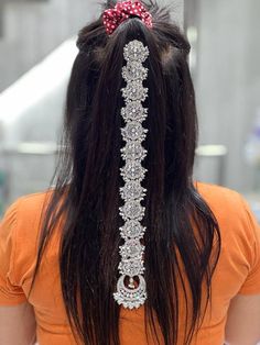 the back of a woman's head with a red bow in her hair and an elaborate necklace on it