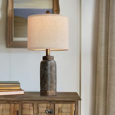 a lamp sitting on top of a wooden table next to a book shelf and window