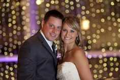 a bride and groom pose for a wedding photo in front of the city lights at night