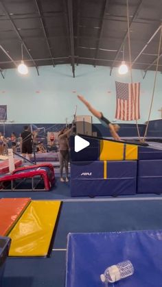 a person on a trampoline in a gym with an american flag hanging from the ceiling