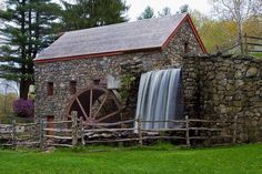 a stone building with a water wheel in front of it and a wooden fence around it