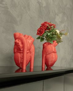 two red vases with roses in them sitting on a shelf next to each other