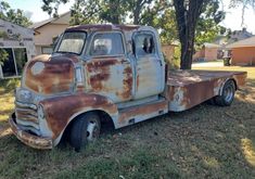 an old rusted out truck parked in the grass next to a tree and house