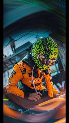 a man in an orange and black racing suit is leaning down on his car while wearing a helmet