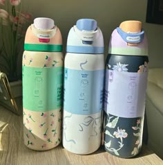 three different colored water bottles sitting on top of a wooden table next to a vase with flowers