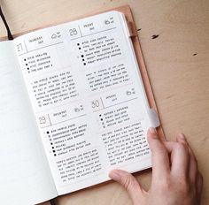 a person is holding a pen and looking at an open notebook on a table with writing in it