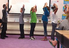 a group of children standing in front of a whiteboard with their hands up to the sky