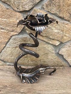 a metal bird sculpture sitting on top of a wooden table next to a stone wall