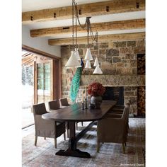 a dining room table with chairs and lights hanging from it's ceiling in front of a stone fireplace