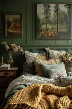 a bed covered in lots of pillows and blankets next to two pictures on the wall