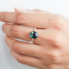 a woman's hand wearing a ring with a blue and green stone on it