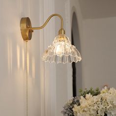 a wall light that is on the side of a wall next to a vase with flowers