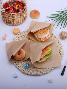 two sandwiches in paper bags sitting on top of a table next to some candies