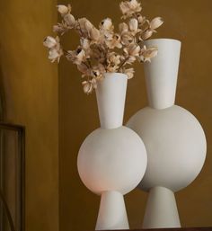 two white vases with flowers in them on a table