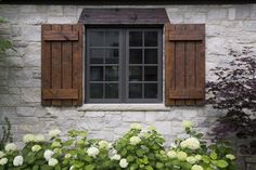 a window with wooden shutters on the side of a stone building surrounded by plants and flowers