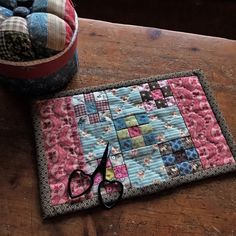 a pair of scissors sitting on top of a wooden table next to a patchwork quilt