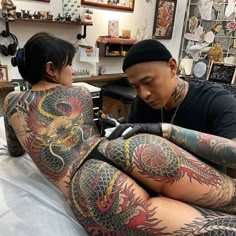 a man and woman with dragon tattoos on their body sitting next to each other in a room