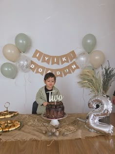 a young boy sitting in front of a cake with the number 2 on it, surrounded by balloons