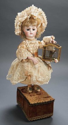 an antique doll holding a bird cage on top of a wooden box with a stuffed animal in it