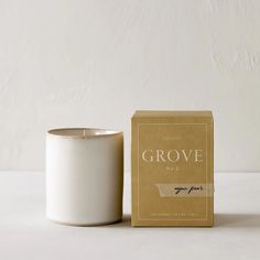 a white candle sitting next to a brown box on a table with a white wall in the background