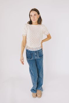 a woman standing in front of a white background wearing blue jeans and a white top