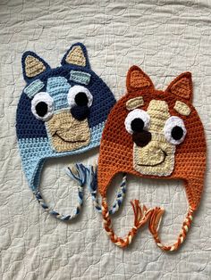 two crocheted hats with eyes and ears on top of a white bed sheet