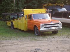 an orange and yellow truck parked next to a white car in front of some trees