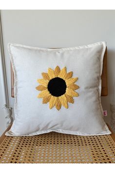 a white pillow with a yellow sunflower embroidered on the front and back, sitting on a wicker chair