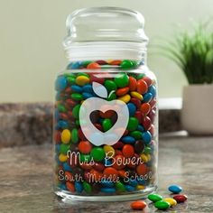 a glass jar filled with lots of colorful candies next to a potted plant