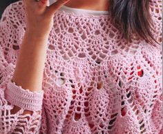 a woman wearing a pink crocheted sweater holding a cell phone