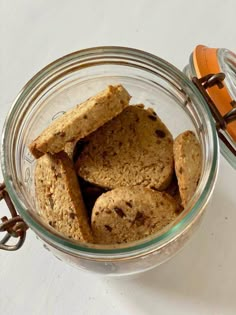 a glass jar filled with cookies sitting on top of a white table next to an orange container