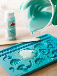 a person pouring blue liquid into a plastic moldy tray on top of a table