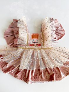 a pink and white dress with gold sequins on the bottom, featuring a doll