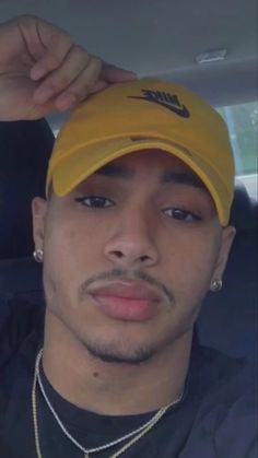 a man wearing a yellow nike hat in the back seat of a car with his hand on his head