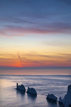 the sun is setting over some rocks in the water