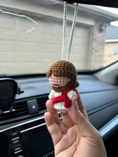 a person holding up a small doll in their hand on the dashboard of a car