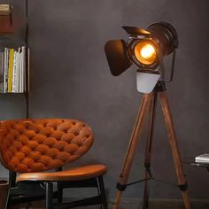 a brown chair sitting next to a lamp on top of a wooden tripod in front of a bookshelf