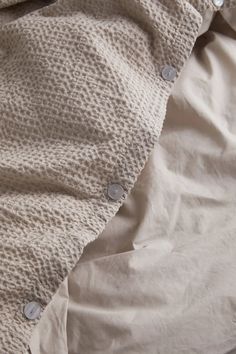 an unmade bed with white sheets and buttons on the pillow cover, which is partially covered by a sheet