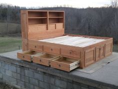 a bed with drawers on top of it sitting in the middle of a field next to a brick wall