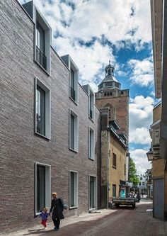 a woman walking down a street with a child in her hand next to a tall brick building