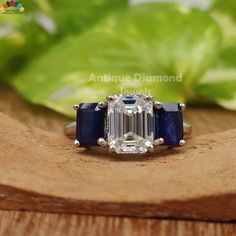 an emerald and sapphire engagement ring on top of a wooden surface with leaves in the background