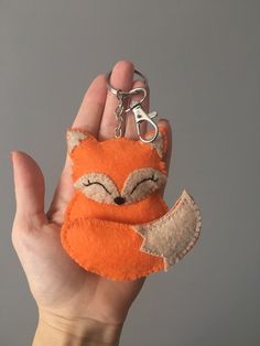 a hand holding a small stuffed animal keychain in the shape of a fox