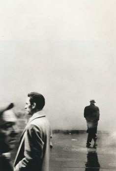 black and white photograph of two men walking in the rain with one man looking at something