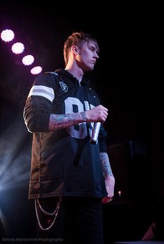 a man with tattoos on his arm holding a microphone and standing in front of some lights