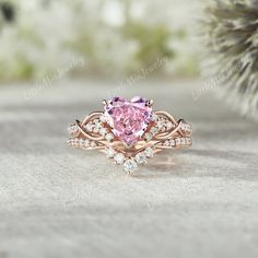 a pink heart shaped diamond ring on top of a pine tree branch with white diamonds