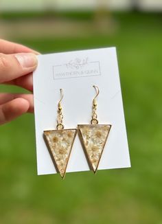 Beautiful handmade upside triangle shaped framed earrings. Created with delicate dried flowers and beautiful gold or silver accents. Available in different colors of flowers, hardware, and accents. Please note that the flowers in these earrings are dried, not pressed. Therefore, they are a bit more dimensional and the tips of the petals may make the surface slightly uneven, as shown in the photos/videos provided.  Made with 18K gold plated, hypoallergenic, lead-free, nickel-free, and cadmium-fre White Triangle Earrings For Gift, Unique Triangle Earrings As A Gift, Triangle Shaped Single Earring As A Gift, Nature-inspired Dangle Earrings With Pressed Flowers, Unique Flower-shaped Earrings With Pressed Flowers, Elegant Resin Flower-shaped Earrings, Unique Flowers, Triangle Shape, Silver Accents