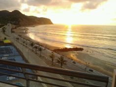 the sun is setting over an ocean beach with tennis courts and palm trees in front of it