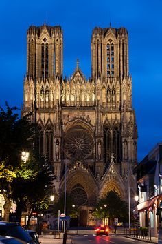 a cathedral lit up at night with cars parked on the street