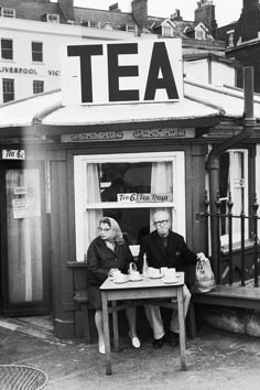 an old photo of two people sitting at a table in front of a tea shop