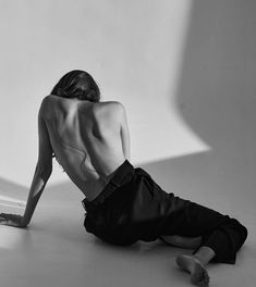 a naked man sitting on the ground in front of a white wall with his back turned to the camera